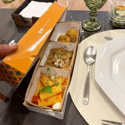 Embalagem executiva retangular sendo utilizada com divisórias internas para servir refeição sofisticada.